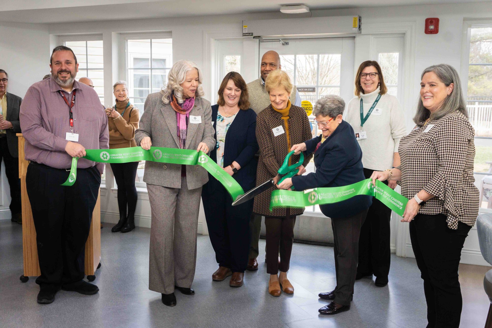 a group of people in business clothing cutting a ribbon with an over-sized pair of scissors.