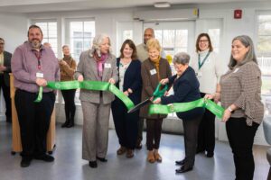 a group of people in business clothing cutting a ribbon with an over-sized pair of scissors.