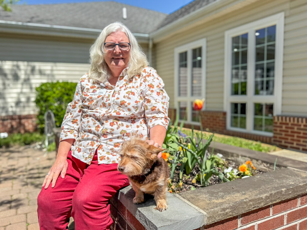 woman sitting on a raised garden bed with a small dog.