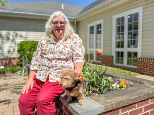 woman sitting on a raised garden bed with a small dog.